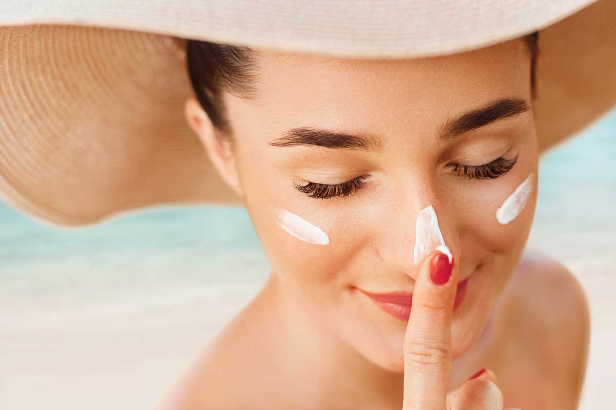 Female in hat applying moisturizing lotion on skin. Beautiful Young woman with sun cream on face.Skin care. Sun protection. Suntan